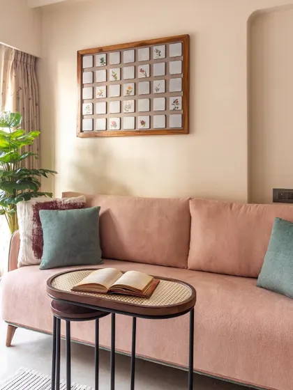 This cozy living room corner uses a blush pink sofa and green accents to feel spacious and serene. The hand-painted tile art piece adds a touch of elegance.