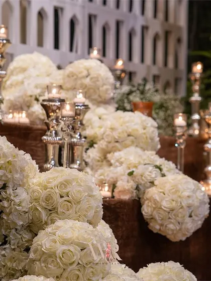A close-up of the cascading white floral installation, showing the density of the rose spheres and the warm glow of the candles on silver stands.