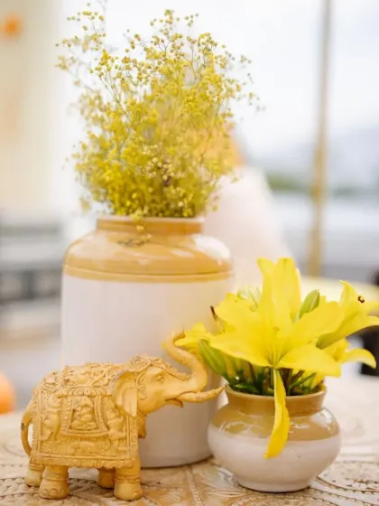 A simple yet elegant centerpiece with yellow lilies and baby's breath in ceramic vases, complemented by a carved elephant figurine.