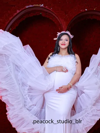 A stunning solo maternity portrait of a woman in a white gown with dramatic ruffled wings, set against a vibrant red heart-shaped backdrop.