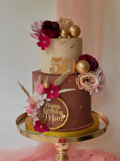 A rich and warm two-tier cake for a 50th birthday. The chocolate and mocha-colored tiers are decorated with silk flowers, dried grasses, and multiple gold toppers.