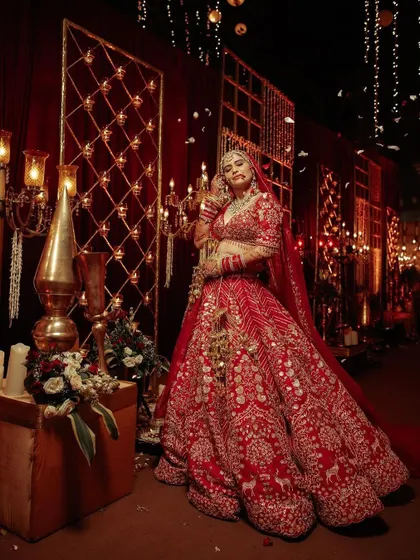 The bride poses against a backdrop of illuminated panels and rich red drapes, a perfect blend of modern lighting and traditional opulence.