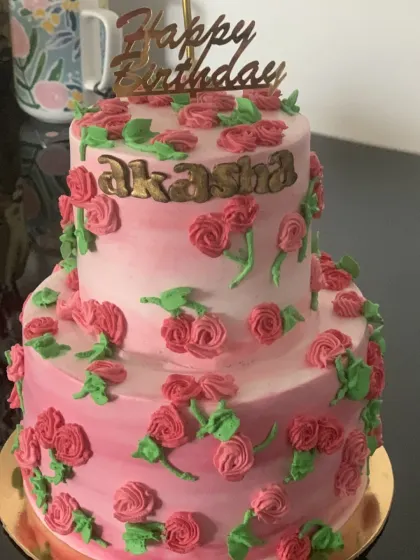 A two-tier floral cake with pink buttercream roses. The ombre effect and gold lettering make this a beautiful choice for a special birthday.