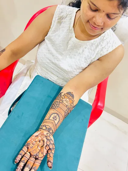 A client admiring her full-arm mehendi. The design features architectural elements and a portrait on the hand.