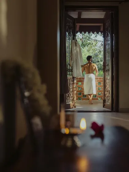 An artistic getting-ready shot of the groom, captured from inside the room as he stands on the balcony, creating a sense of anticipation.