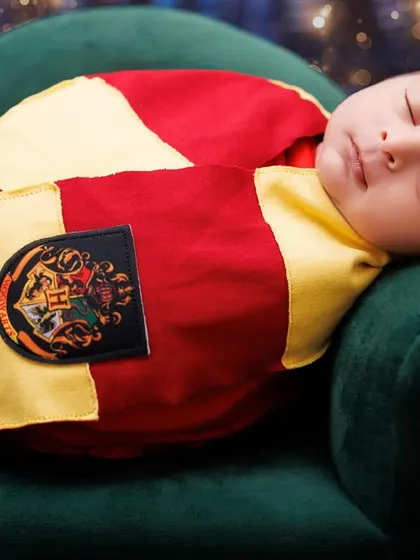 A sleeping newborn dressed as Harry Potter, resting on a green armchair. A close-up shot capturing their peaceful expression.