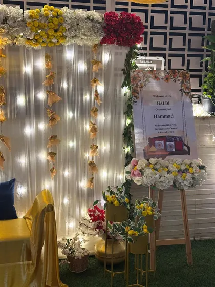 The welcome area for the Haldi ceremony, featuring a personalized sign on an easel, decorated with flowers that match the main backdrop.