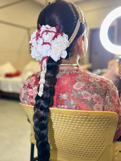 A behind the scenes look at the placement of a beautiful floral headpiece on a traditional bridal braid, showing the artistry involved.