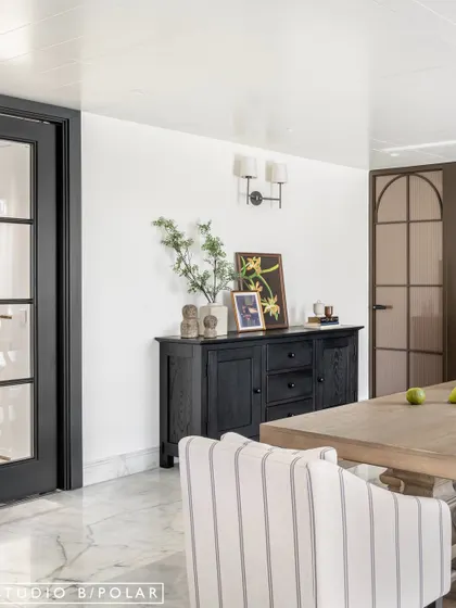 A black sideboard provides a strong visual anchor and practical storage. The mix of modern and traditional elements, like the French doors and contemporary wall sconces, creates a balanced design.