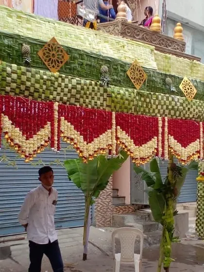 Here is a closer look at the craftsmanship involved in a traditional *chappra*. The roof is made of intricately woven leaves, while the front is decorated with beautiful red and white floral hangings, blending natural materials with classic floral art.