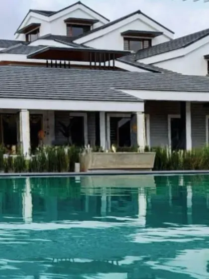 Reflections of sophistication. A classic farmhouse design is beautifully mirrored in the calm waters of the adjacent pool, blending architecture, water, and sky.