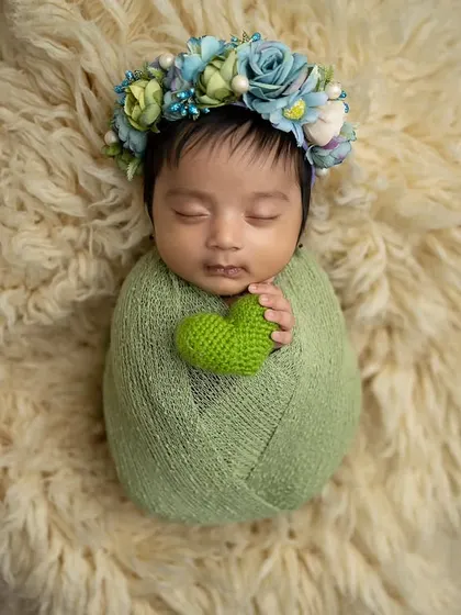 Another angle of the green swaddle pose on the fur rug, showing the baby holding a crocheted green heart.