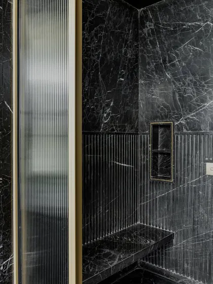 In this washroom, we used fluted and smooth black marble to create a space that is both dramatic and tactile, with a built-in shower bench for added comfort.