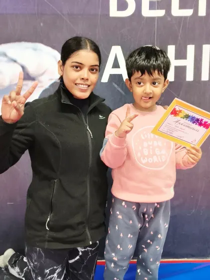 A happy toddler and her coach celebrate a new certificate with matching peace signs.