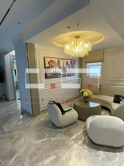 A real photo of a luxurious living room in the DLF Belaire project, featuring curved sofas, a grand chandelier, and classic wall molding.