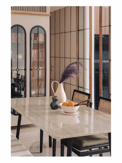 This view shows how our custom dining furniture integrates with other elements like the arched glass library. The marble table and cane chairs provide a light, natural counterpoint to the dark metal frames, creating a balanced and elegant space.