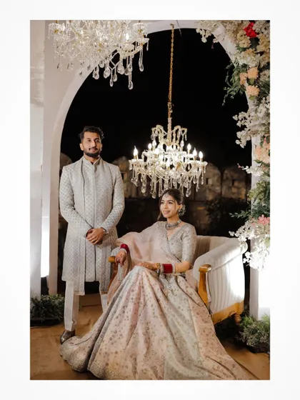 A formal portrait of the couple seated under a grand chandelier at their Jaipur wedding reception.