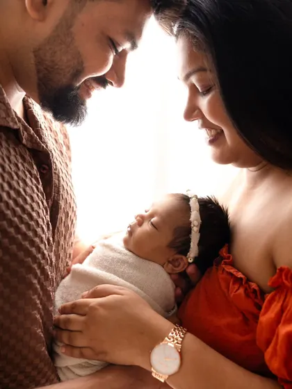 Framed by her loving parents, this newborn sleeps peacefully. This silhouette-style shot uses natural light to create a soft, artistic, and intimate family portrait.