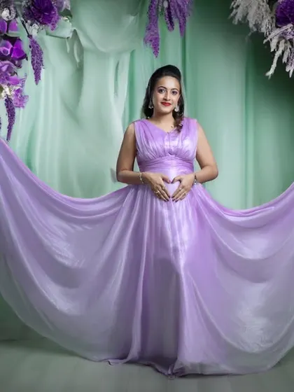 A dreamy and dramatic maternity portrait. The mom-to-be stands in a beautiful lavender gown, surrounded by a stunning arch of purple and white flowers.