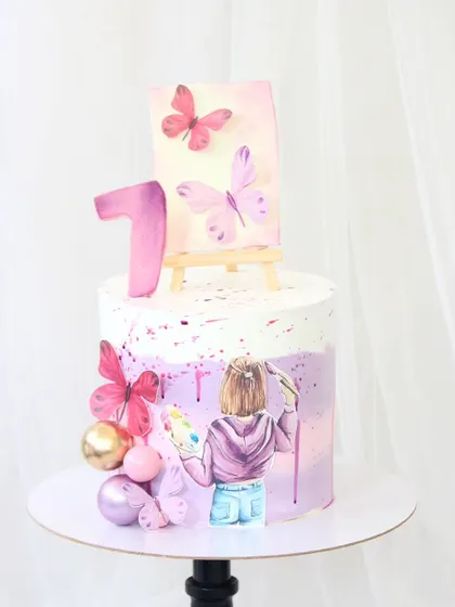 A pretty pastel cake for a first birthday. The design features a hand-painted artist with a palette, an easel with a butterfly painting, and delicate wafer paper butterflies.
