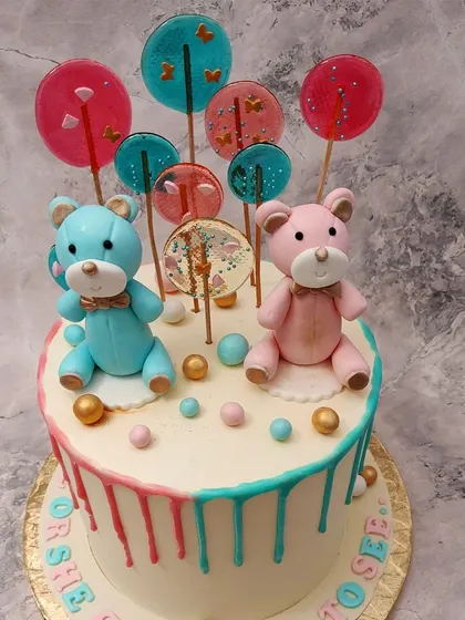 We create a sweet surprise with this teddy bear gender reveal drip cake. A pink and a blue teddy bear sit among colorful lollipops, while pink and blue drips run down the sides, making the reveal a truly delightful moment.