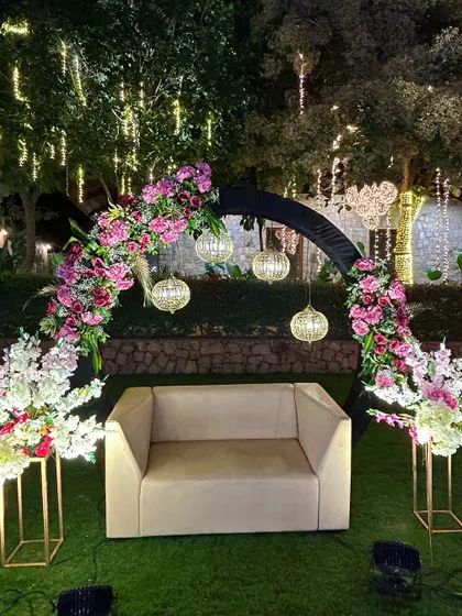 A cozy photo booth for a sangeet, featuring a floral-draped arch, hanging lanterns, and comfortable seating.