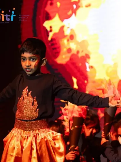 A boy stands with arms outstretched against a fiery backdrop, embodying the element of Agni with a powerful pose.