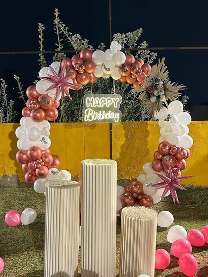 An elegant outdoor ring decoration set up on a lawn. This setup features a balloon arch in chrome and white, with star-shaped foil balloons and a 'Happy Birthday' neon sign.