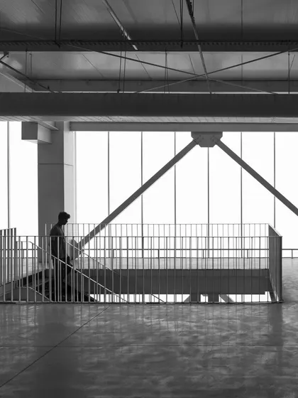 The interior of the T Works prototyping facility. The industrial aesthetic, with its exposed steel structure and polished concrete floors, is bathed in diffused natural light, creating a vast, minimalist, and honest space perfect for innovation.