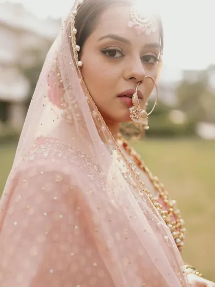 A soft, sunlit portrait of the bride, Apurva, her gaze gentle and captivating, framed by her delicate pink veil.