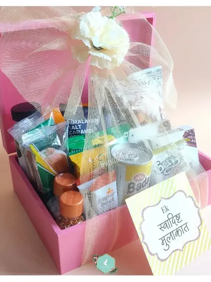 A "Swaadisht Mulakat" (tasty meeting) hamper designed to welcome wedding guests. This pink wooden box is filled with a variety of Indian snacks and drinks, ensuring guests feel comfortable and cared for during their stay.
