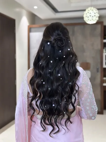 A dreamy and romantic hairstyle. These soft, flowing waves are dotted with delicate pearls and feature a beautiful rose bun, creating a look that is pure elegance.