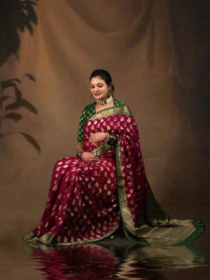A traditional and graceful maternity portrait. The client is seated, wearing a beautiful magenta and green saree, creating a culturally rich and elegant image against a classic painted backdrop.