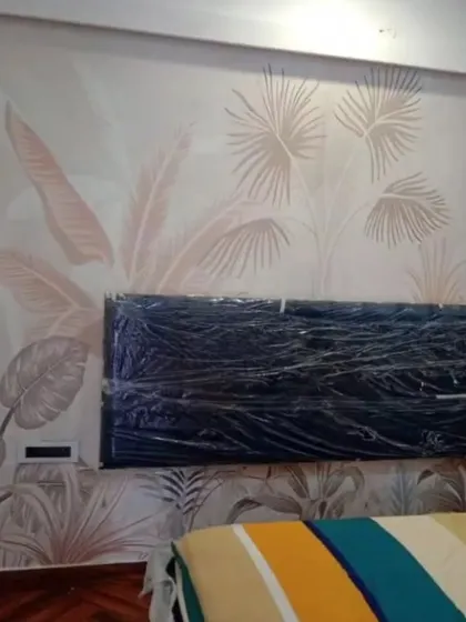A soft, muted botanical wallpaper being installed behind a headboard. This design is perfect for creating a serene and understated elegance in a bedroom.