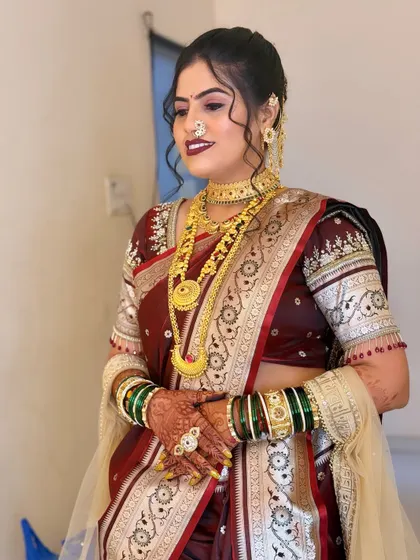 A full view of the bride's maroon saree look. The green and gold bangles provide a beautiful contrast against the deep red of her saree.