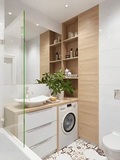 A practical and space-efficient bathroom design that integrates the washing machine next to the vanity. The light wood cabinetry provides ample storage, and the patterned floor tiles add a decorative touch.