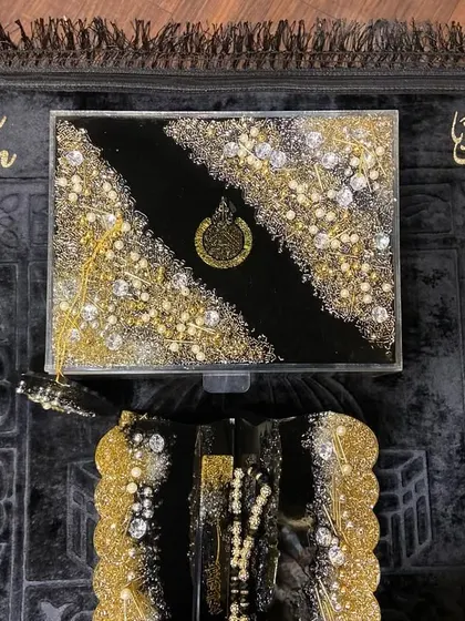A top-down view of the complete black and gold gift set, showing the Quran box, holder, and personalized prayer mat.