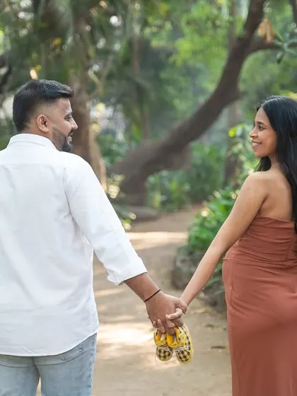 A simple and classic maternity pose. The couple walks hand-in-hand through a park, with the focus on their connection and the tiny baby shoes they carry, symbolizing their journey ahead.