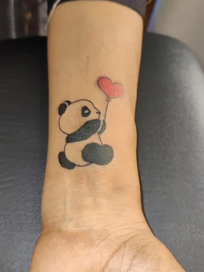 A cute and simple panda tattoo on the wrist, holding a red heart-shaped balloon. This shows that minimalist tattoos can also be playful and colorful.