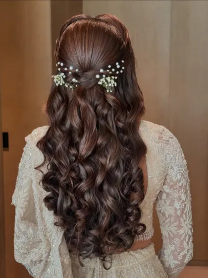 A classic half-up style with perfectly defined curls. The hair is twisted back and adorned with delicate baby's breath and pearls for a timeless, romantic look.