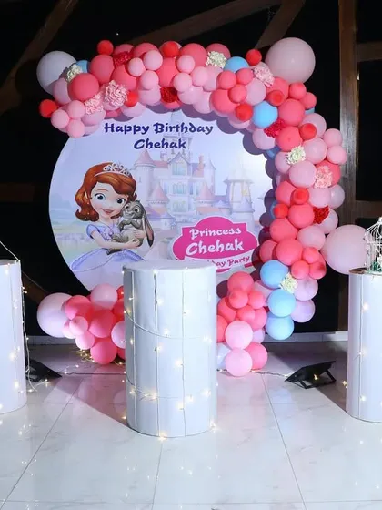 A "Sofia the First" princess-themed cake-cutting area. The setup includes a custom circular backdrop and a pink and red balloon arch.