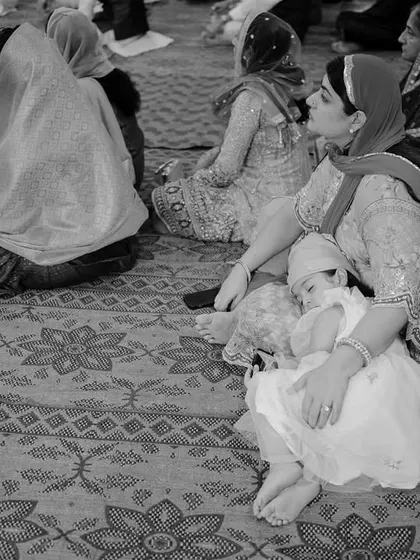 A touching black and white photo of a young child asleep in her mother's lap during a ceremony. This quiet, candid moment beautifully illustrates the peaceful trust between a mother and child.