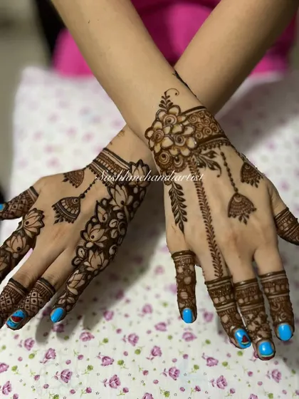 A beautiful jewelry-style mehndi with hanging jhumkas and lotus flowers. The blue nail polish makes the henna design stand out.