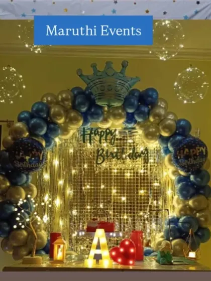A royal-themed birthday table decoration with a blue and gold balloon arch, a crown, and fairy lights for a magical touch.
