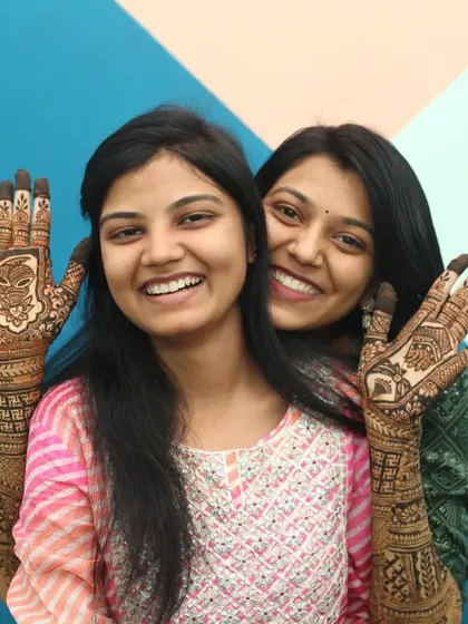 A happy portrait of two sisters posing together to show off their completed mehandi designs. This is a great example of a relaxed, fun group photo that families will cherish.