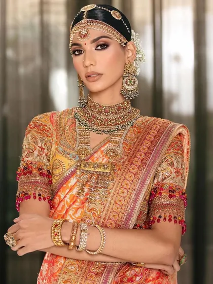 A traditional bridal look with a rich orange and red saree. The makeup features a classic winged liner and a bold bindi, celebrating heritage with refined technique.