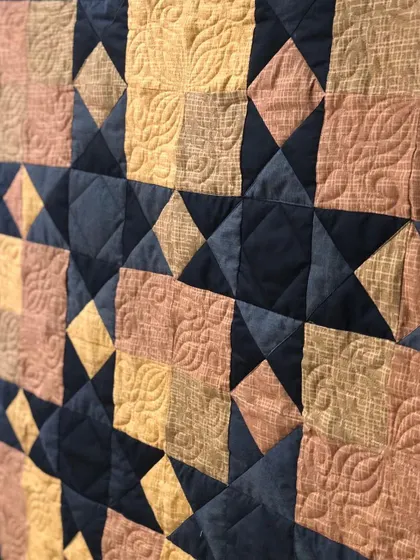 A close-up of the Sawtooth Star memory quilt, showing the detailed feather-and-leaf longarm quilting pattern.