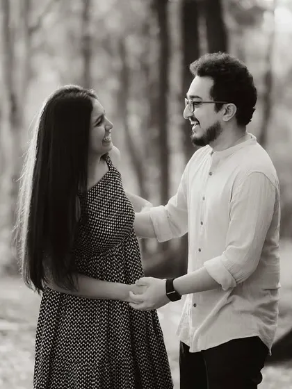 A black and white photo of the couple holding hands and talking in the forest. The focus is on their interaction, creating a sense of intimacy and quiet conversation.