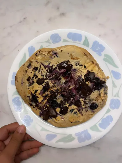 A close-up of my homemade protein pancake with blueberries and chocolate. Getting creative in the kitchen is a great way to stick to your nutrition goals without feeling like you're on a restrictive diet.