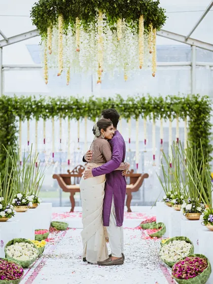 A candid moment of a couple embracing within a lush, green mandap, showcasing the joy of the occasion.
